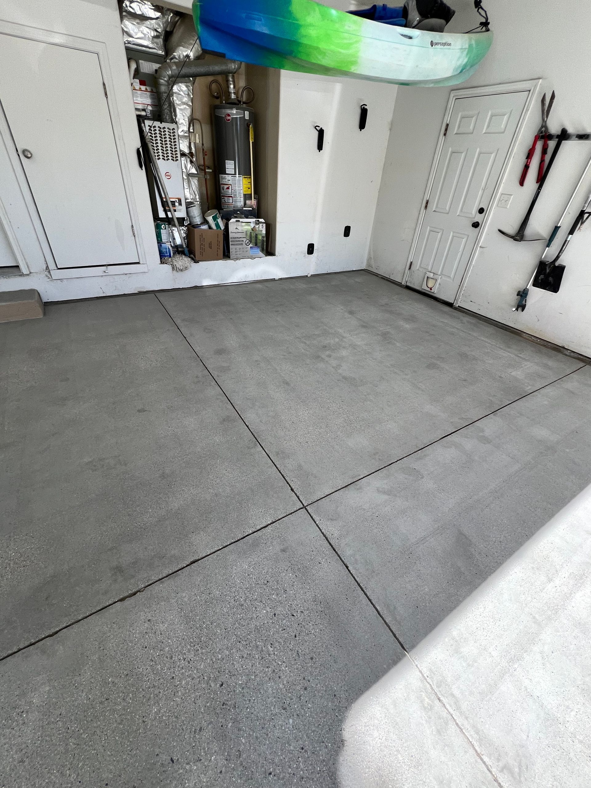 A garage interior showing a concrete floor with gray speckled coating, a water heater, and a kayak hanging overhead.