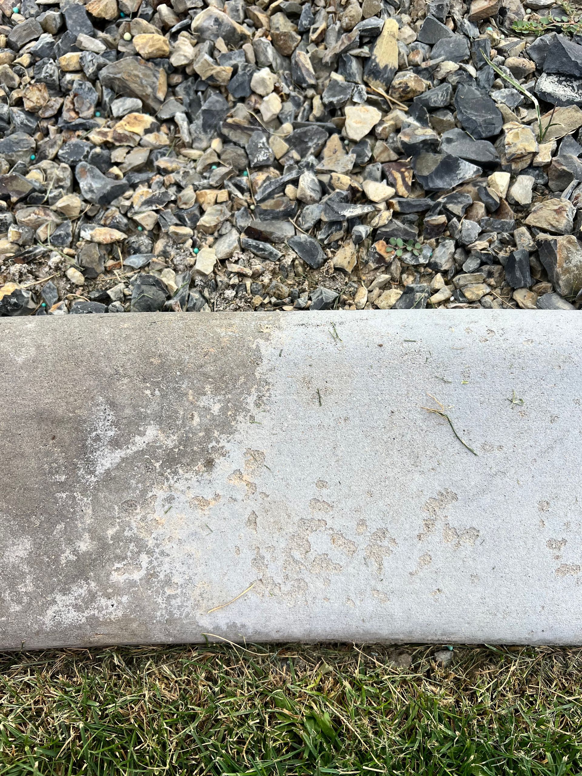 A concrete curb edge split between a dark, weathered section on the left and a clean, light section on the right.