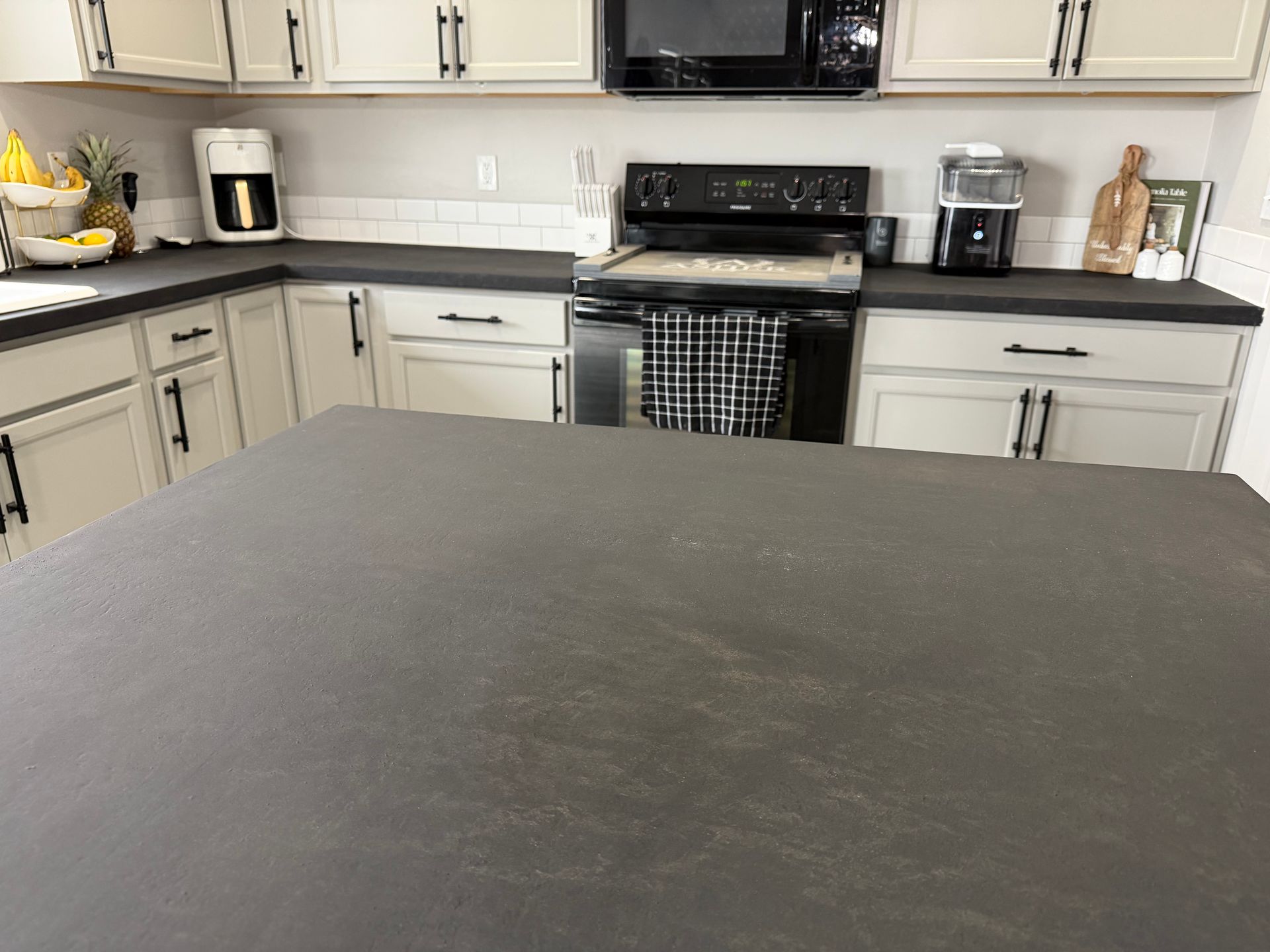 A modern kitchen with light gray cabinets, a black island countertop, white subway tile backsplash, and black appliances.