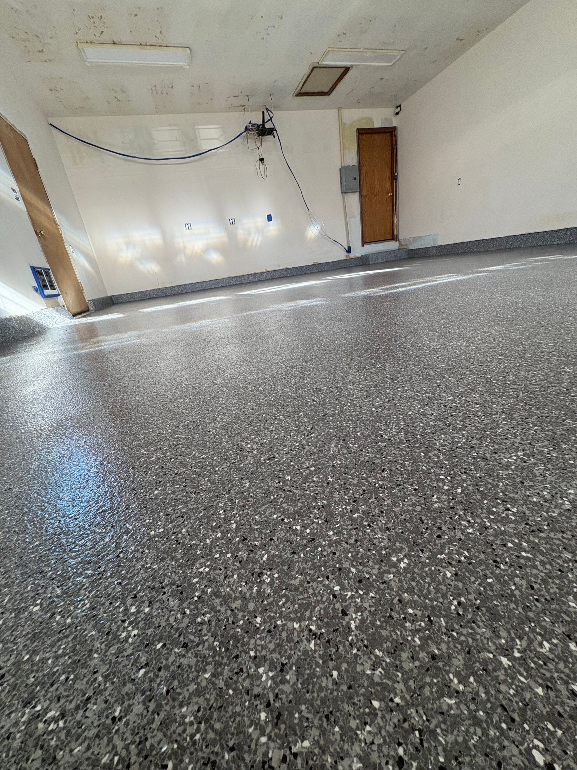 A newly installed grey and white speckled epoxy garage floor with a glossy finish in an empty room.
