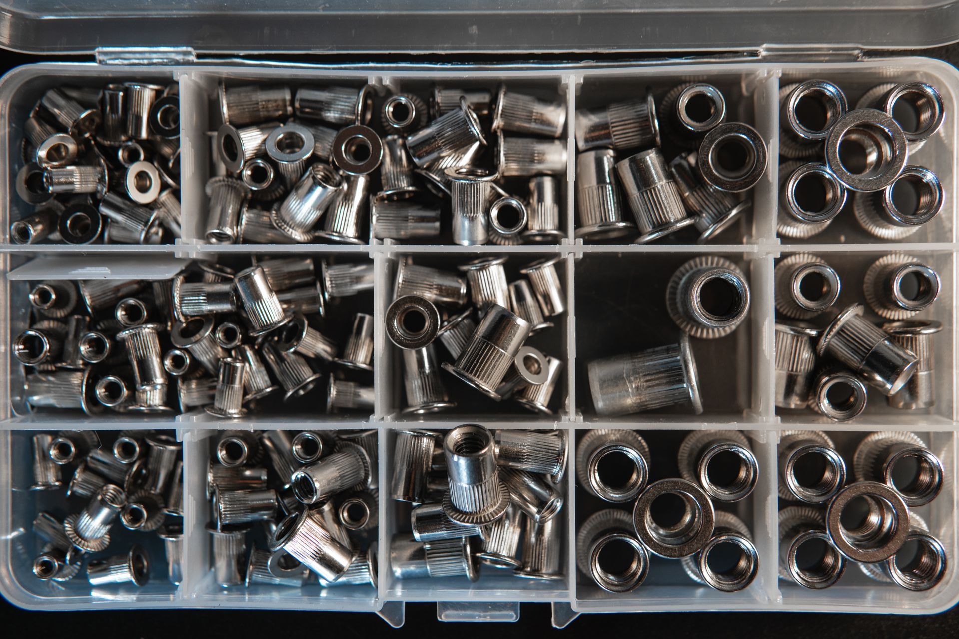 A variety of threaded metal rivet inserts neatly organised within a container.