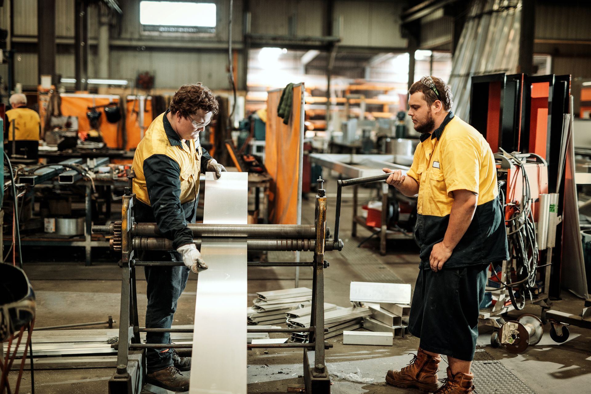 Two metal fabricators in yellow shirts operating machinery in a factory with safety gear Two metal fabricators in yellow shirts operating machinery in a factory with safety gear