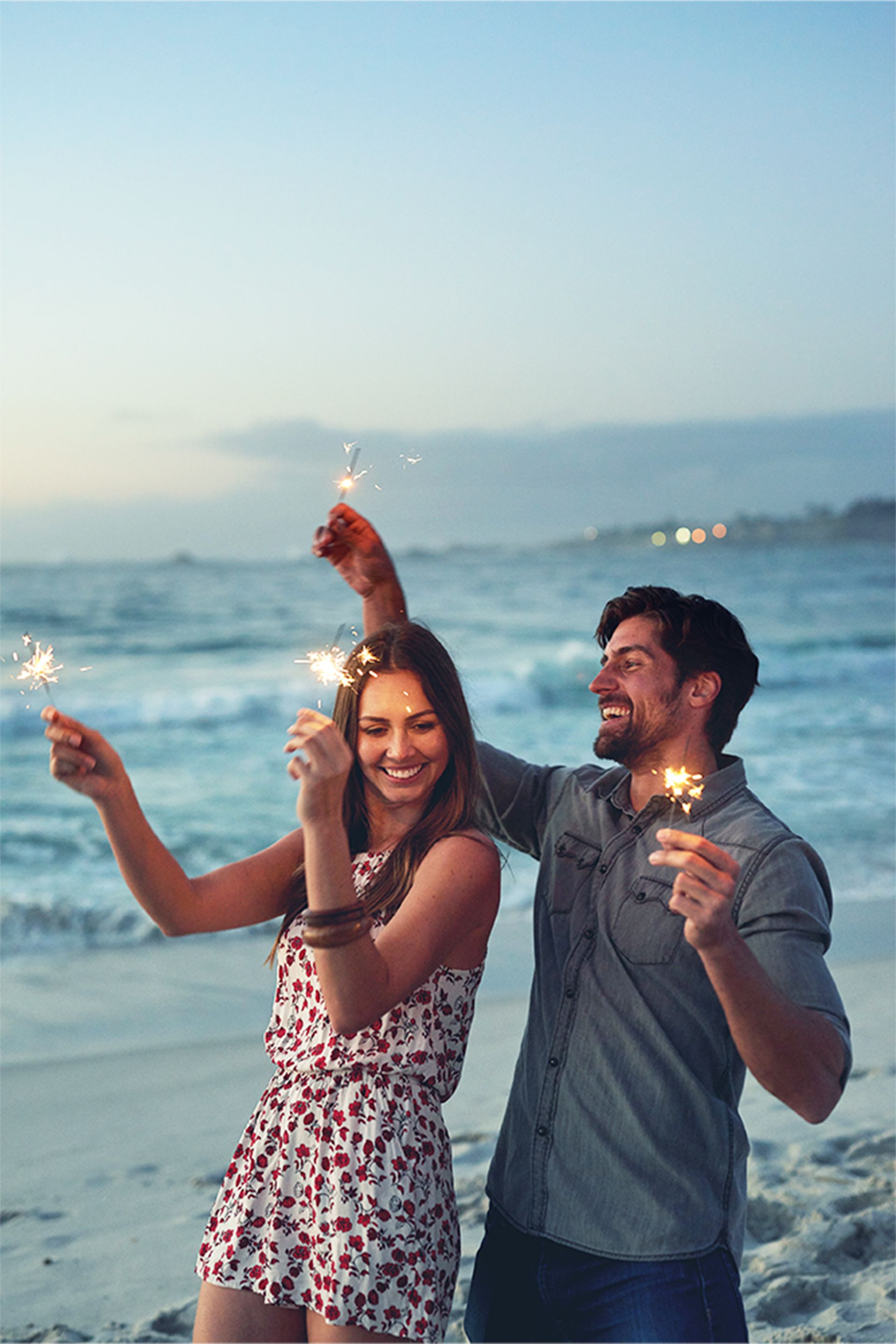 A man and a woman are holding sparklers on the beach.
