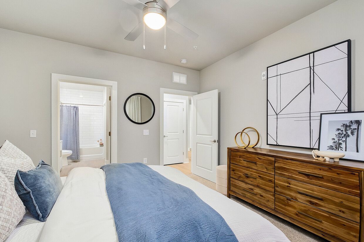 A bedroom with a bed , dresser , mirror and potted plant.