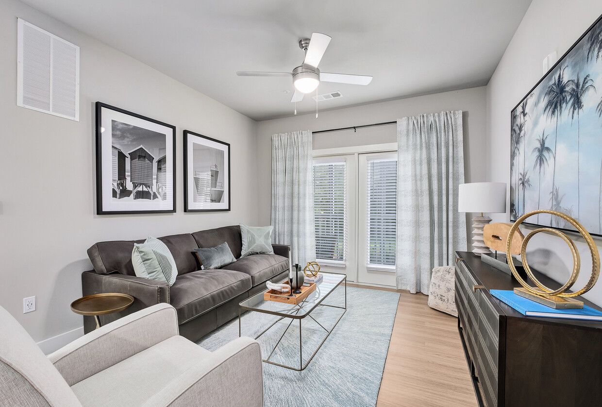 A living room with a couch , chair , coffee table and ceiling fan.