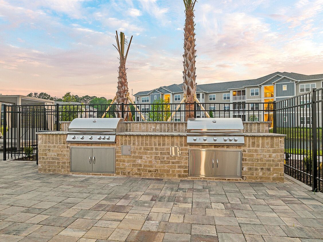 Two grills are sitting on top of a brick patio next to a fence.