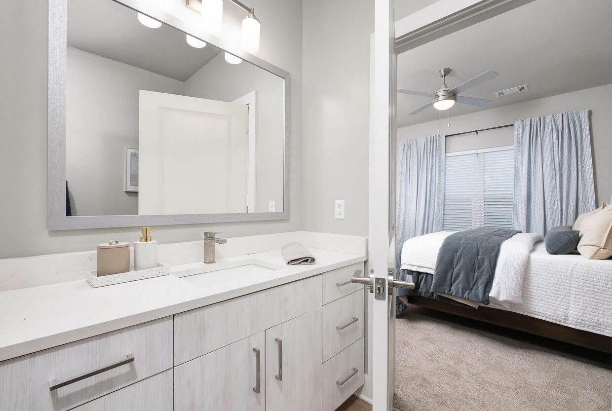 A bathroom with a sink and a mirror next to a bedroom with a bed.