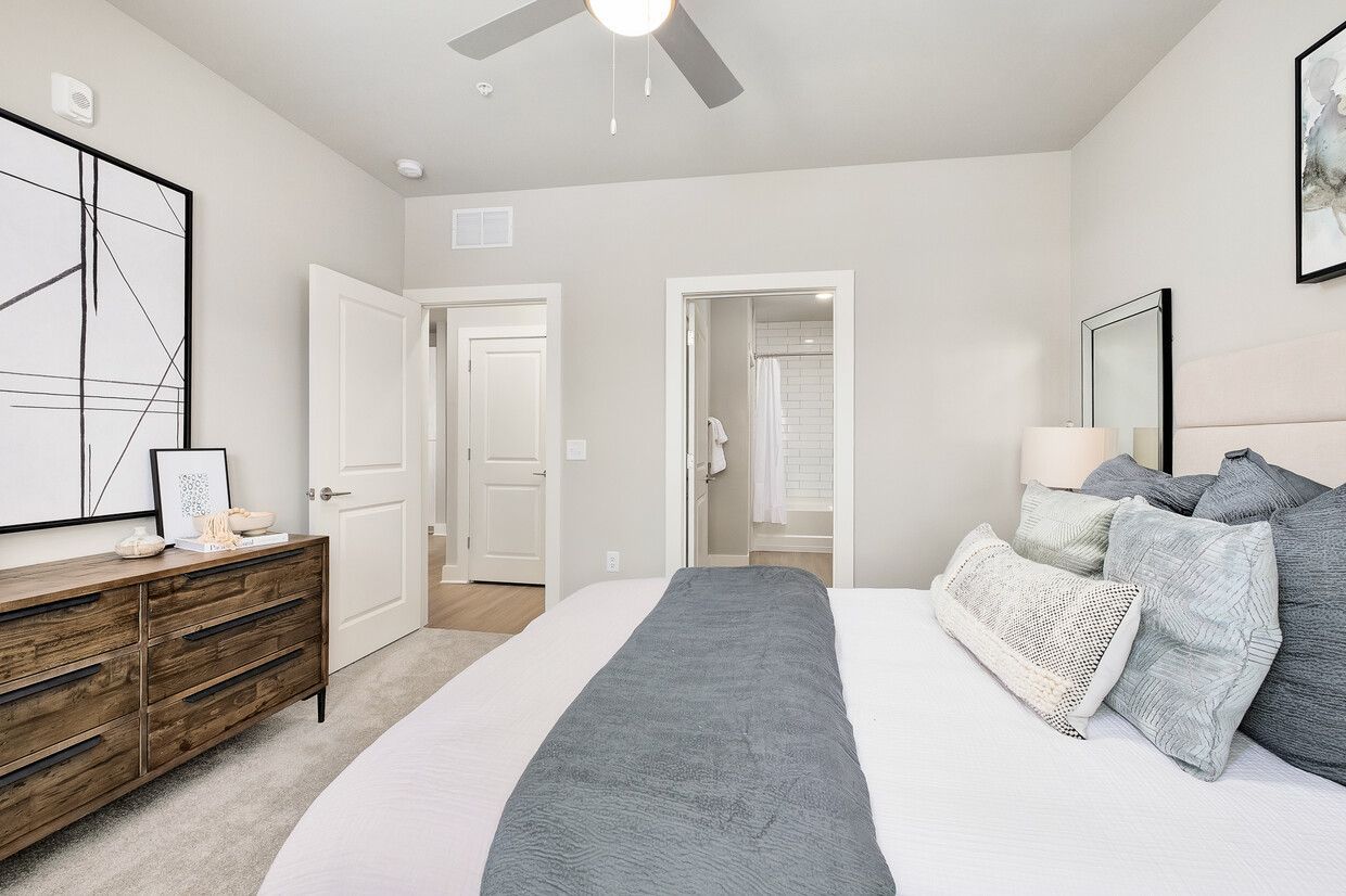 A bedroom with a bed , dresser , mirror and ceiling fan.