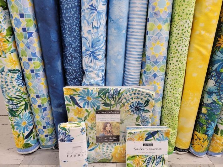 View of various quilts with blue and yellow tones and flowers, from a local quilt shop.