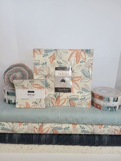 Beige, dark blue, and baby blue tone quilts rolled on a desk at a local quilt shop.