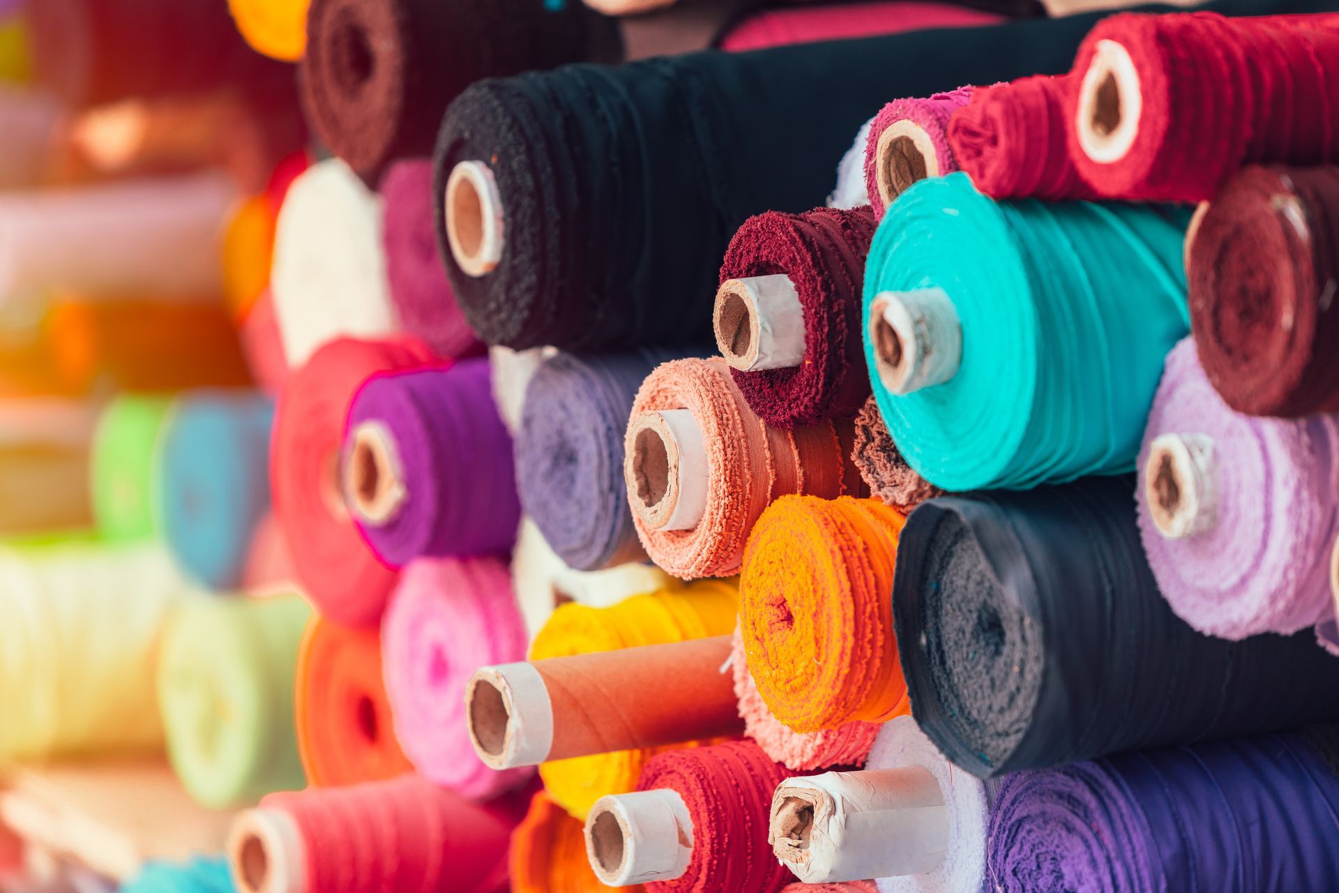 Colorful fabric rolls stacked in textile shop with vibrant assorted cloth for sewing.