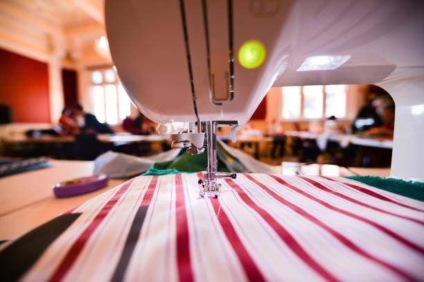 Sewing machine stitching striped fabric in a busy workshop for detailed custom textile work projects.