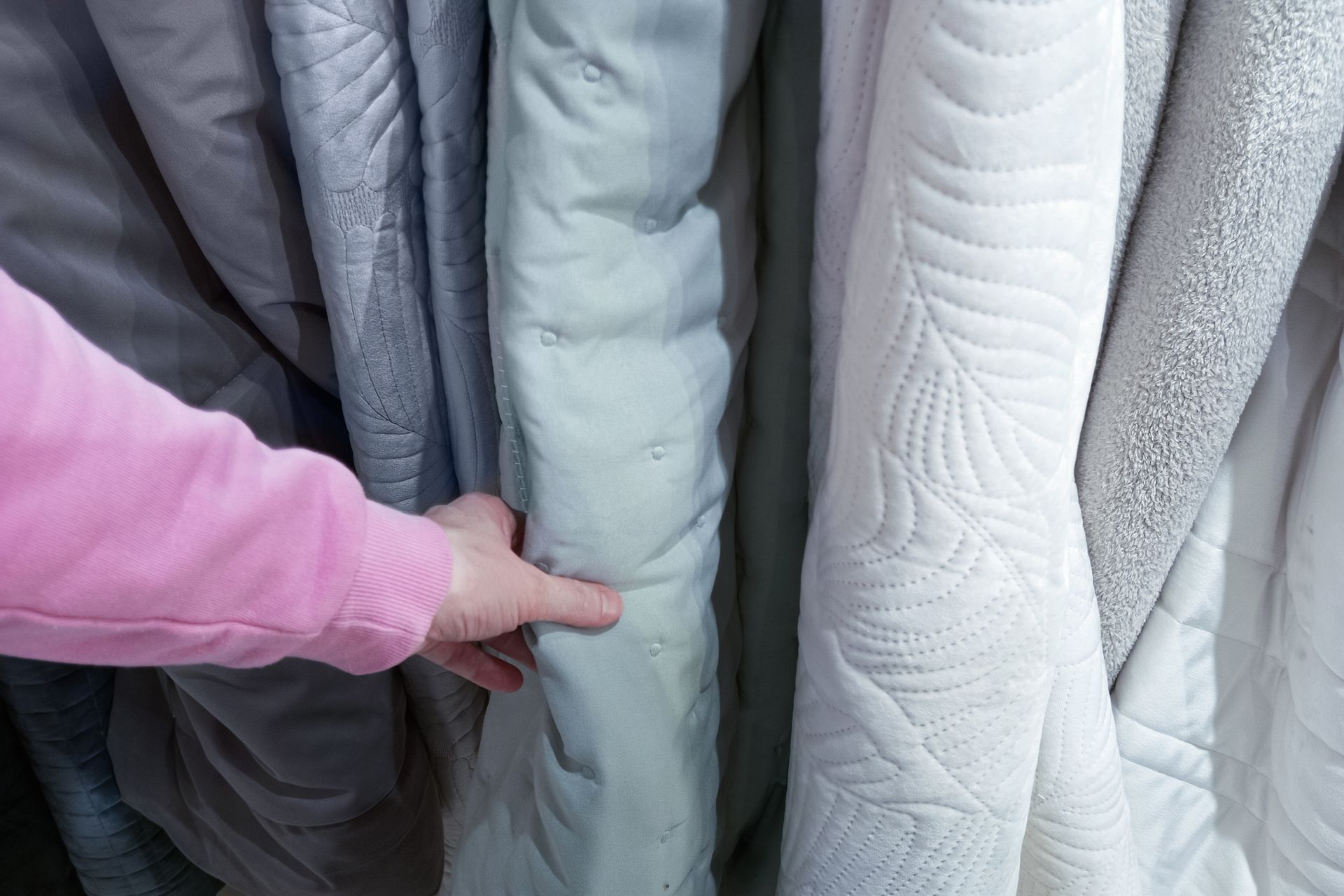 A man touches the bedspreads hanging on a rail in the store.