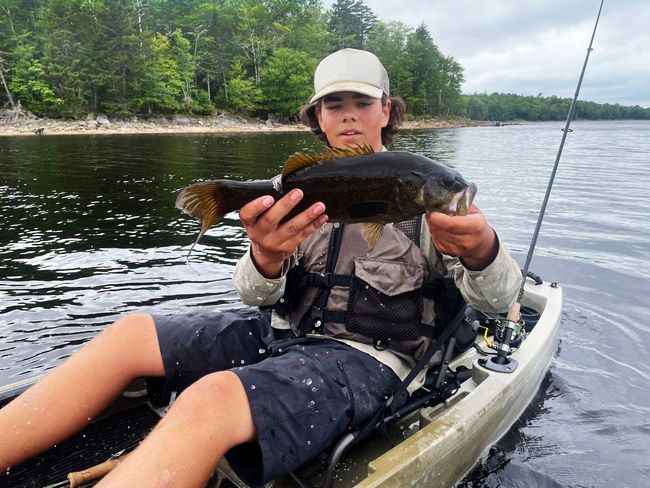A boy in a kayak is holding a fish in his hands