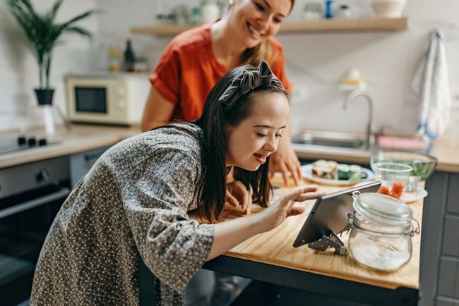 A woman and a girl are looking at a tablet in a kitchen.