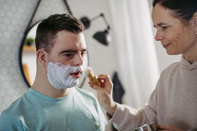 A woman is shaving a man's face in a bathroom.