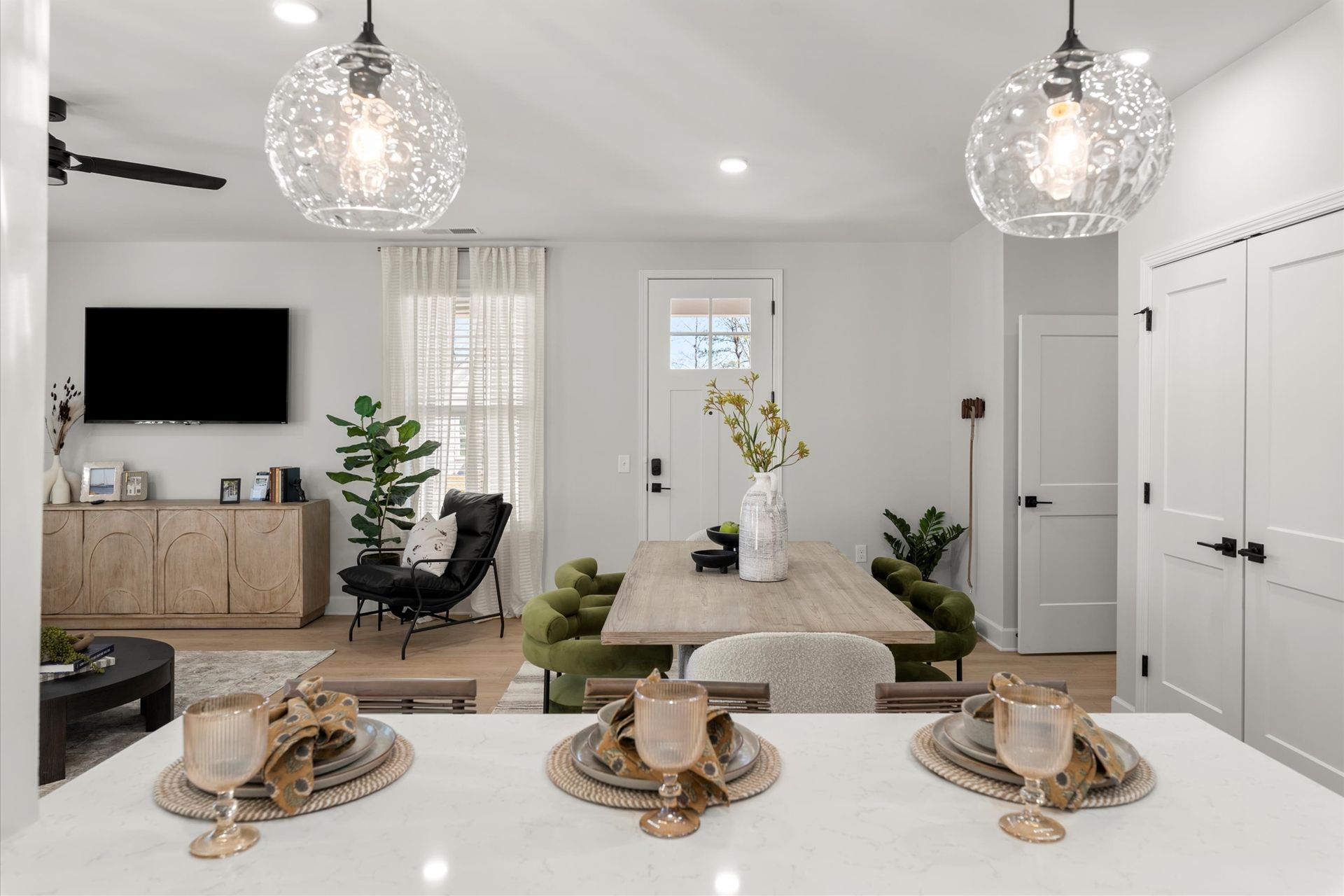 Bright dining area with modern light fixtures, table set with three place settings.