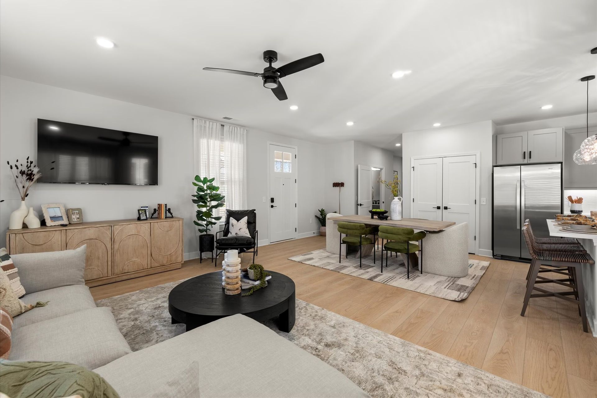 Modern living room with white walls, light wood floors, and open kitchen featuring a large island.