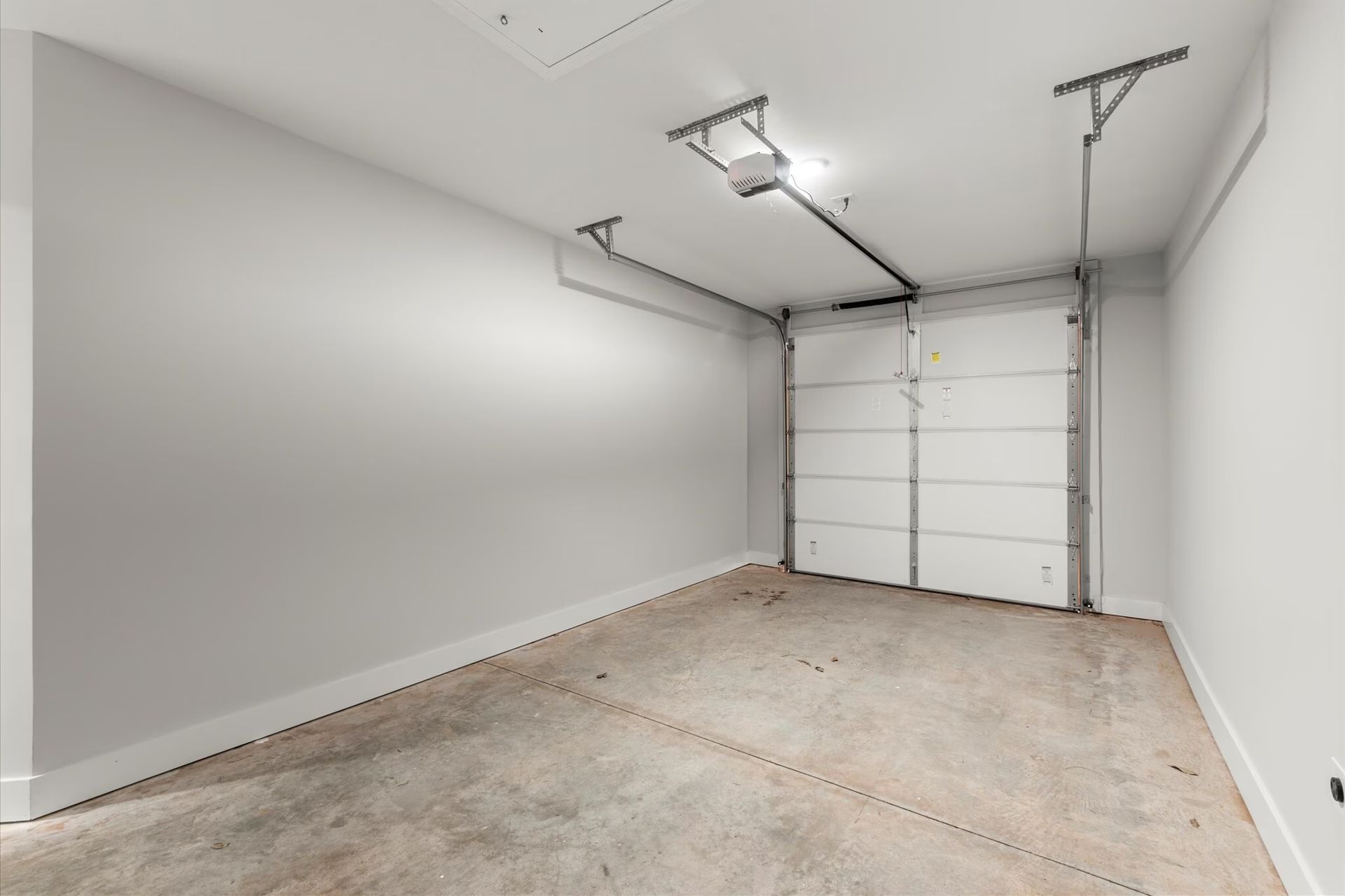 Empty, white-walled garage with a closed white garage door at the back. Concrete floor.