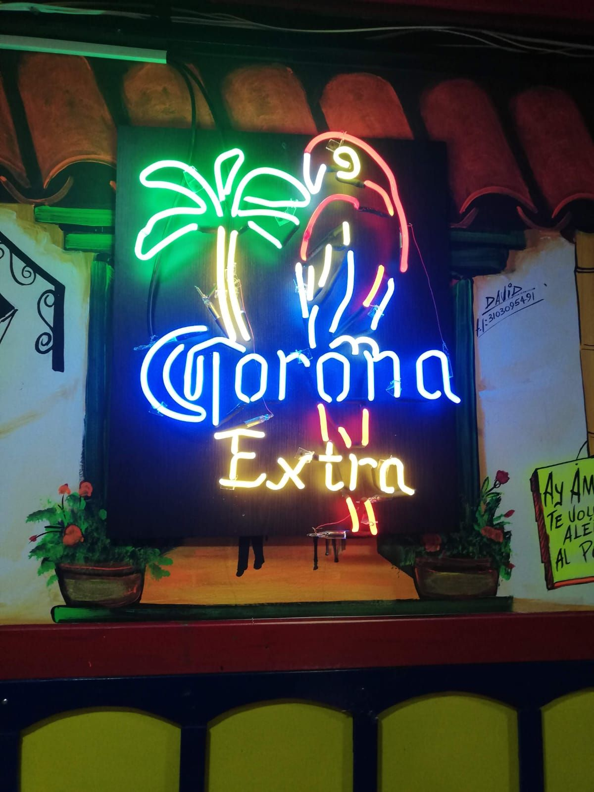 Letrero de neón de cerveza Corona Extra con una palmera y un loro, iluminado en verde, azul y rojo.