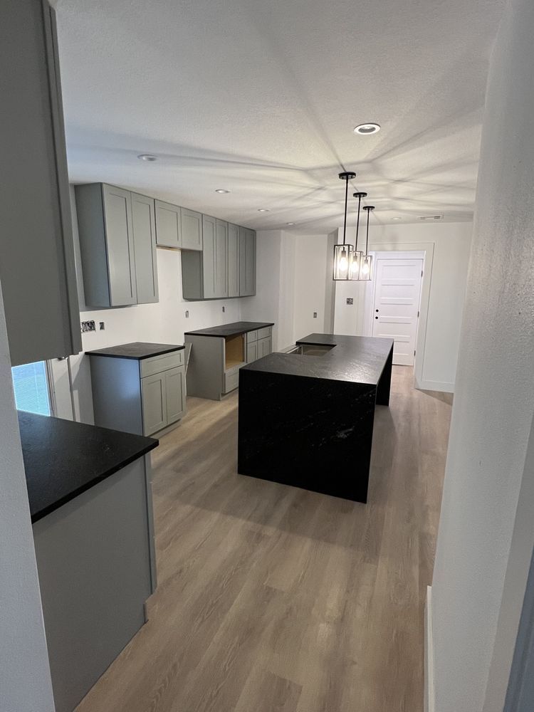 Bright modern kitchen with white cabinets, gray floors, black island, and stainless steel appliances