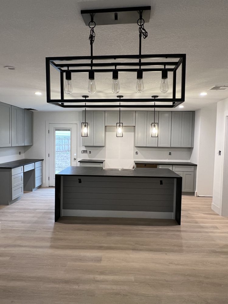 Modern kitchen with gray cabinets, light wood floors, and a black island under a geometric pendant light fixture