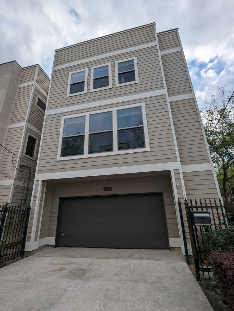 Three-story beige townhouse with a large black garage door and small front gate