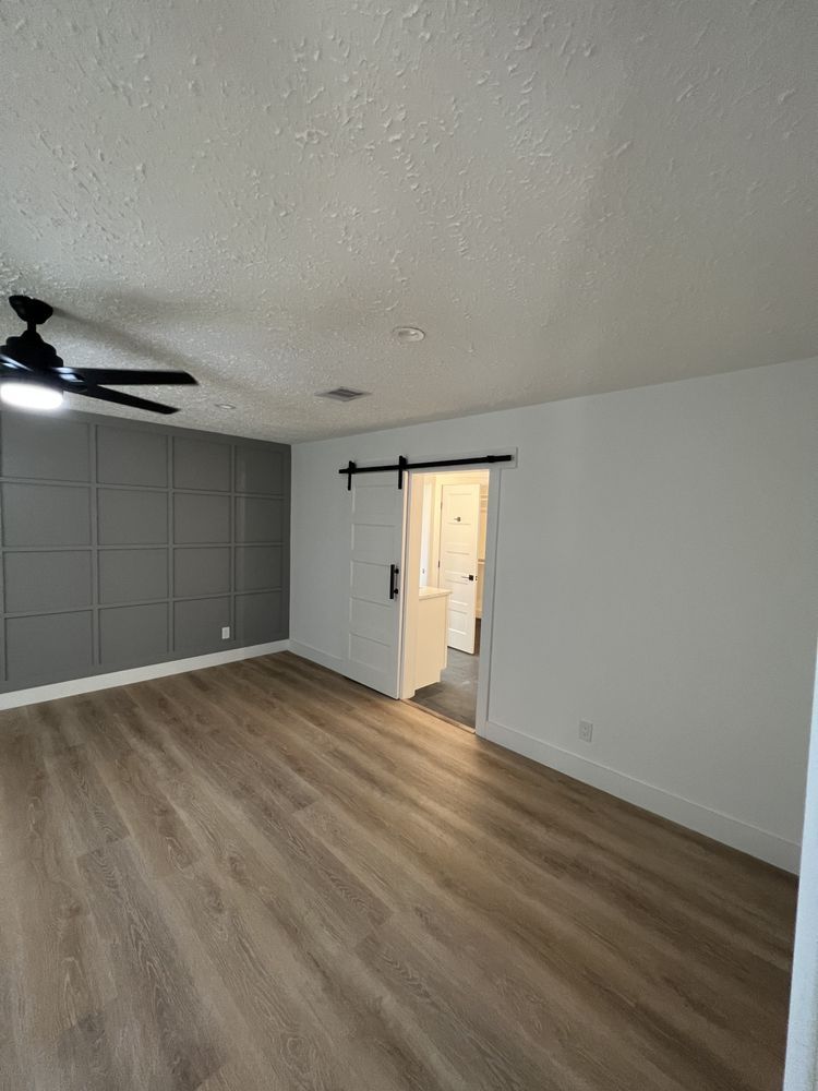 Empty modern bedroom with gray walls, wood floor, ceiling fan, and open door to hallway