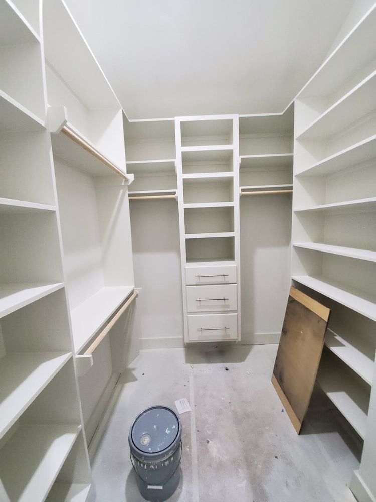 White walk-in closet with built-in shelving, drawers, and a bucket on the floor under construction