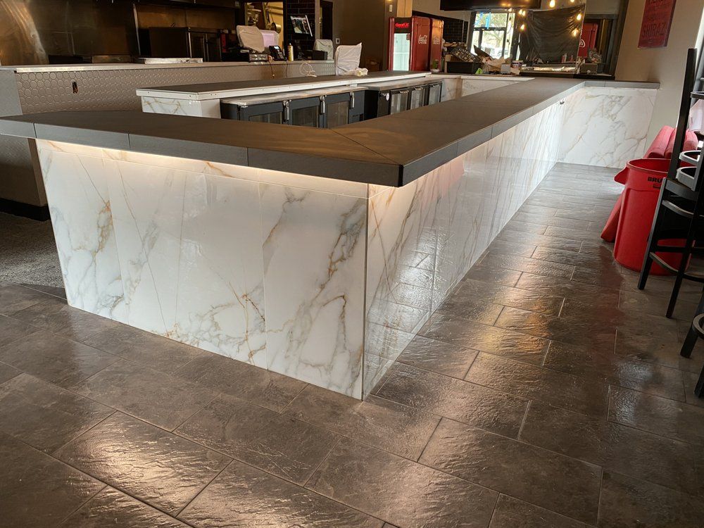 Marble-front restaurant bar with dark wood countertop and tile floor, viewed from an angle