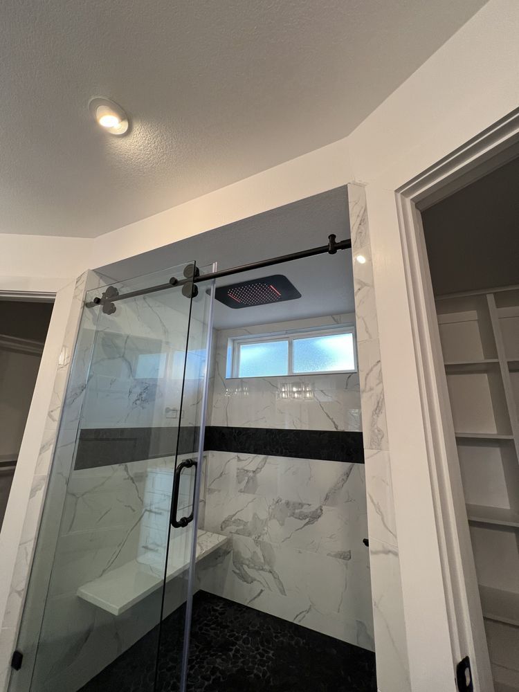 Glass shower stall with black fixtures and marble-look tile walls in a bathroom