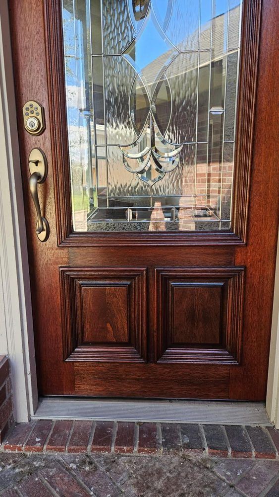 Wooden front door with frosted glass panel and brass handle, framed by brick threshold