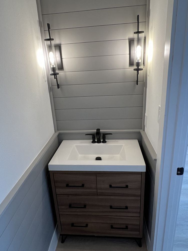 Small bathroom vanity with white sink, dark wood cabinet, gray walls, and wall sconces.