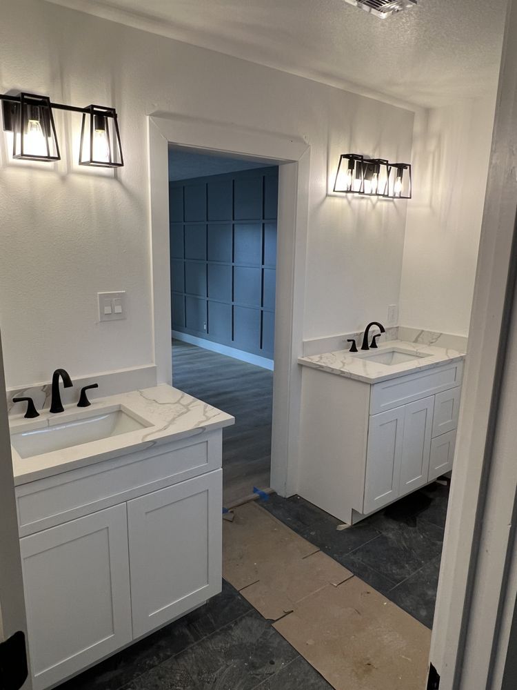 Modern bathroom with two white vanities, black sconces, and an open doorway to a tiled room