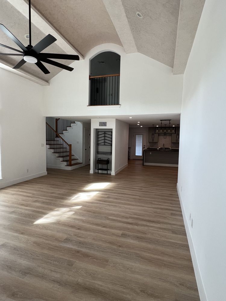 Spacious empty living room with vaulted ceiling, ceiling fan, wood floors, staircase, and open kitchen area