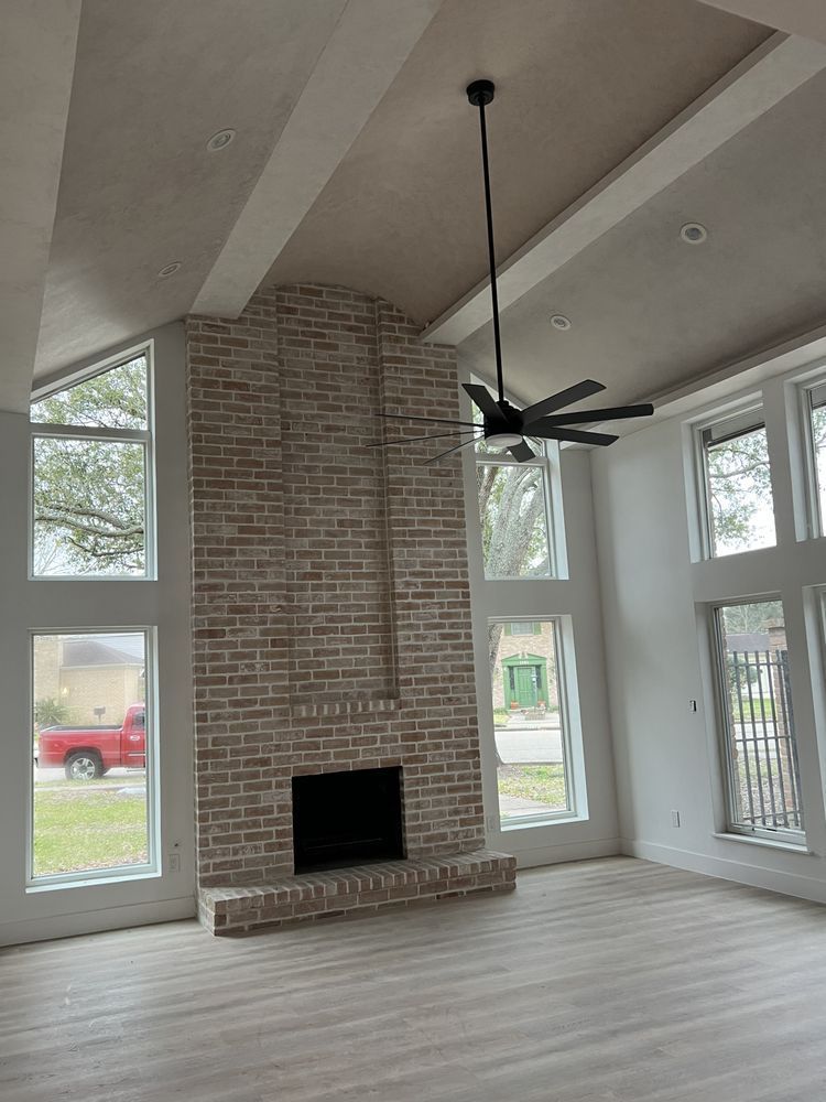 Modern living room with vaulted ceiling, brick fireplace, ceiling fan, and large windows