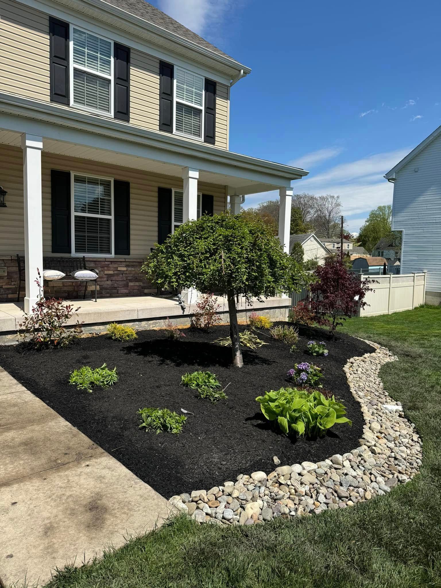 Landscaped front yard with a tree, black mulch, and stone border in front of a house.