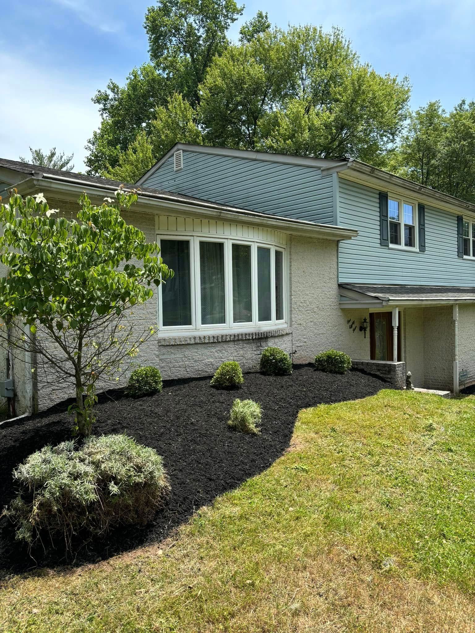 House with green tile roof, white trim, bay window, black mulch landscaping, and green grass.