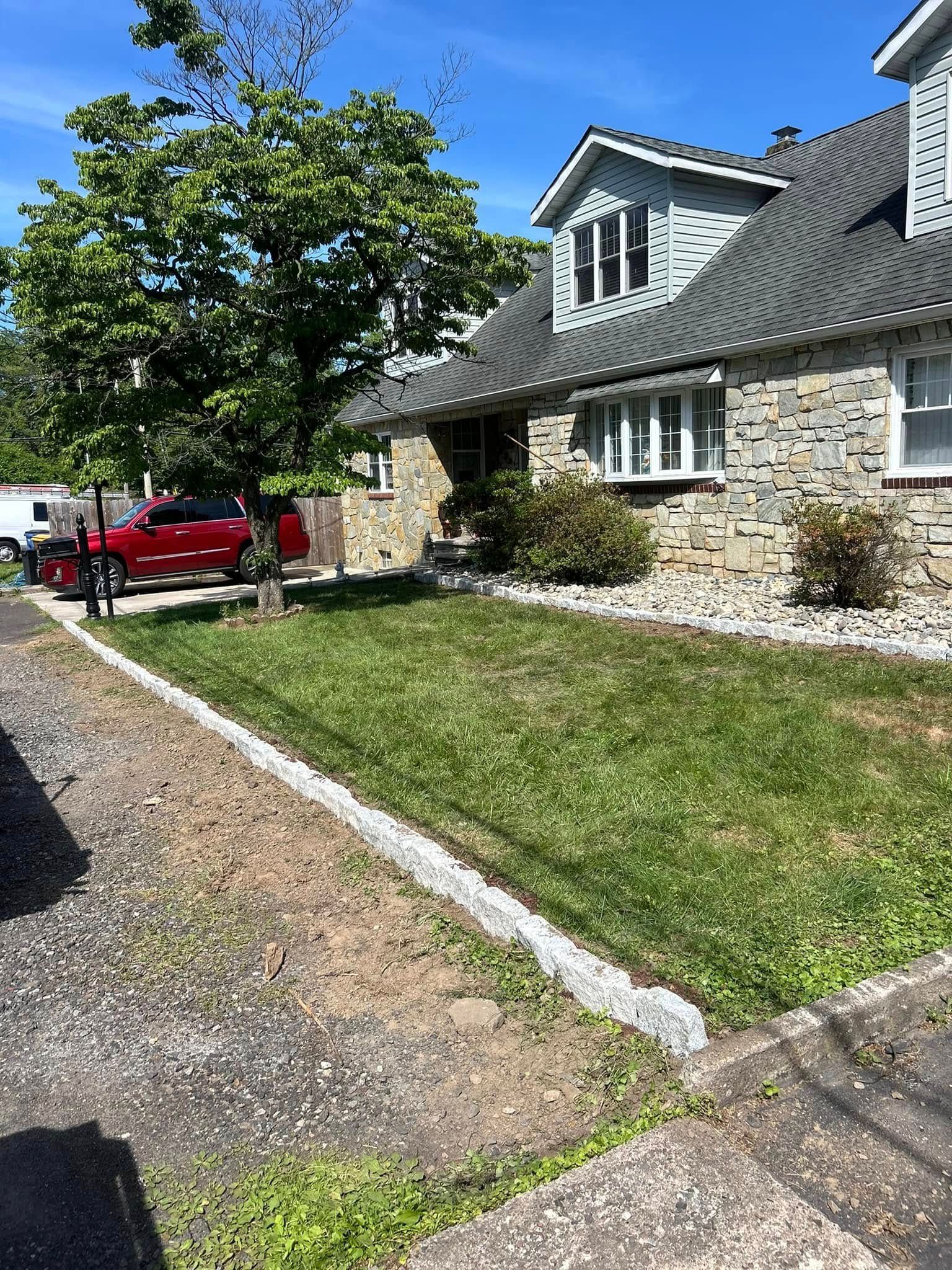 Stone house with green lawn, tree, and red car on a sunny day.