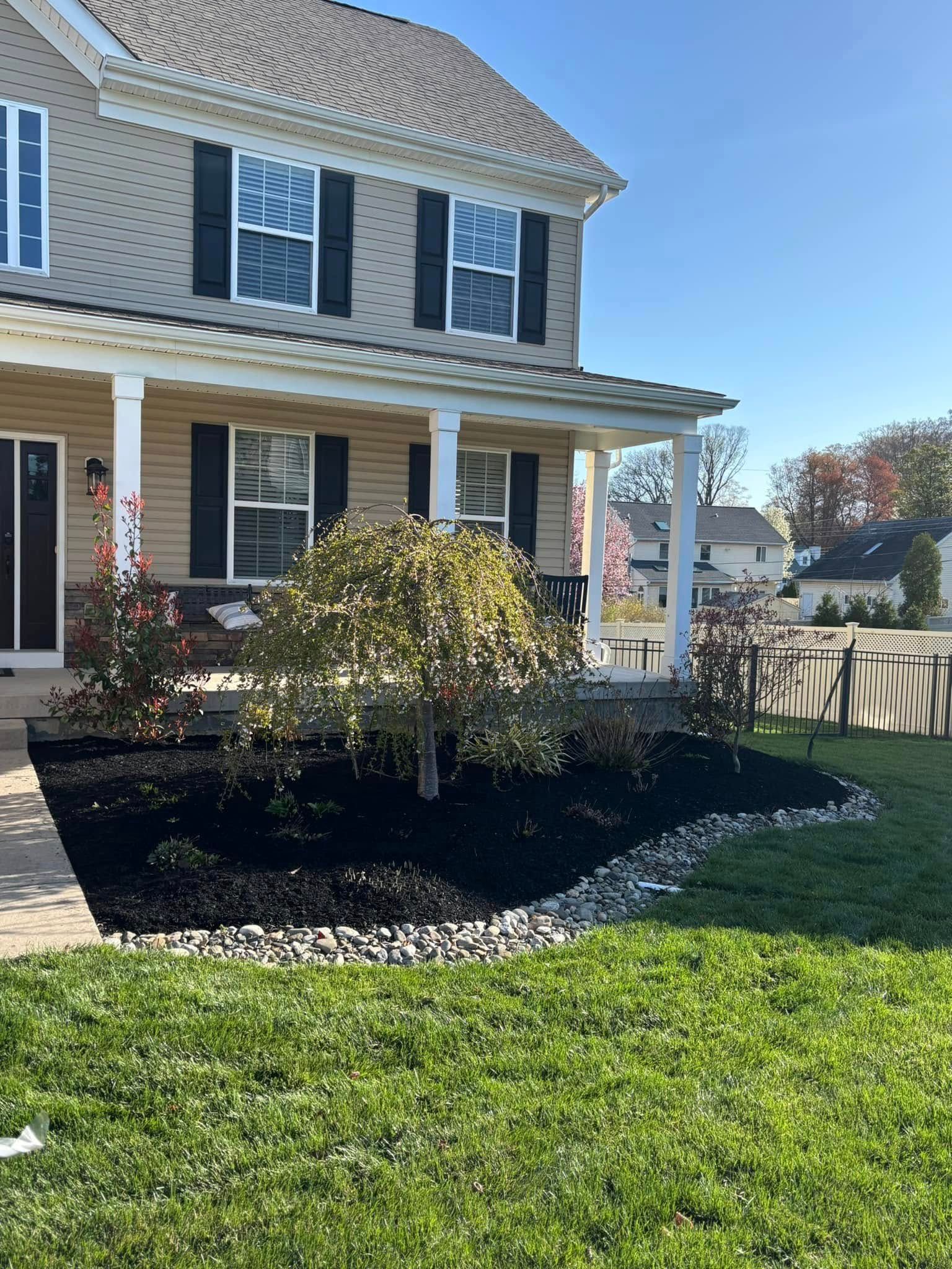 House with a porch and landscaped front yard with a weeping tree and black mulch.