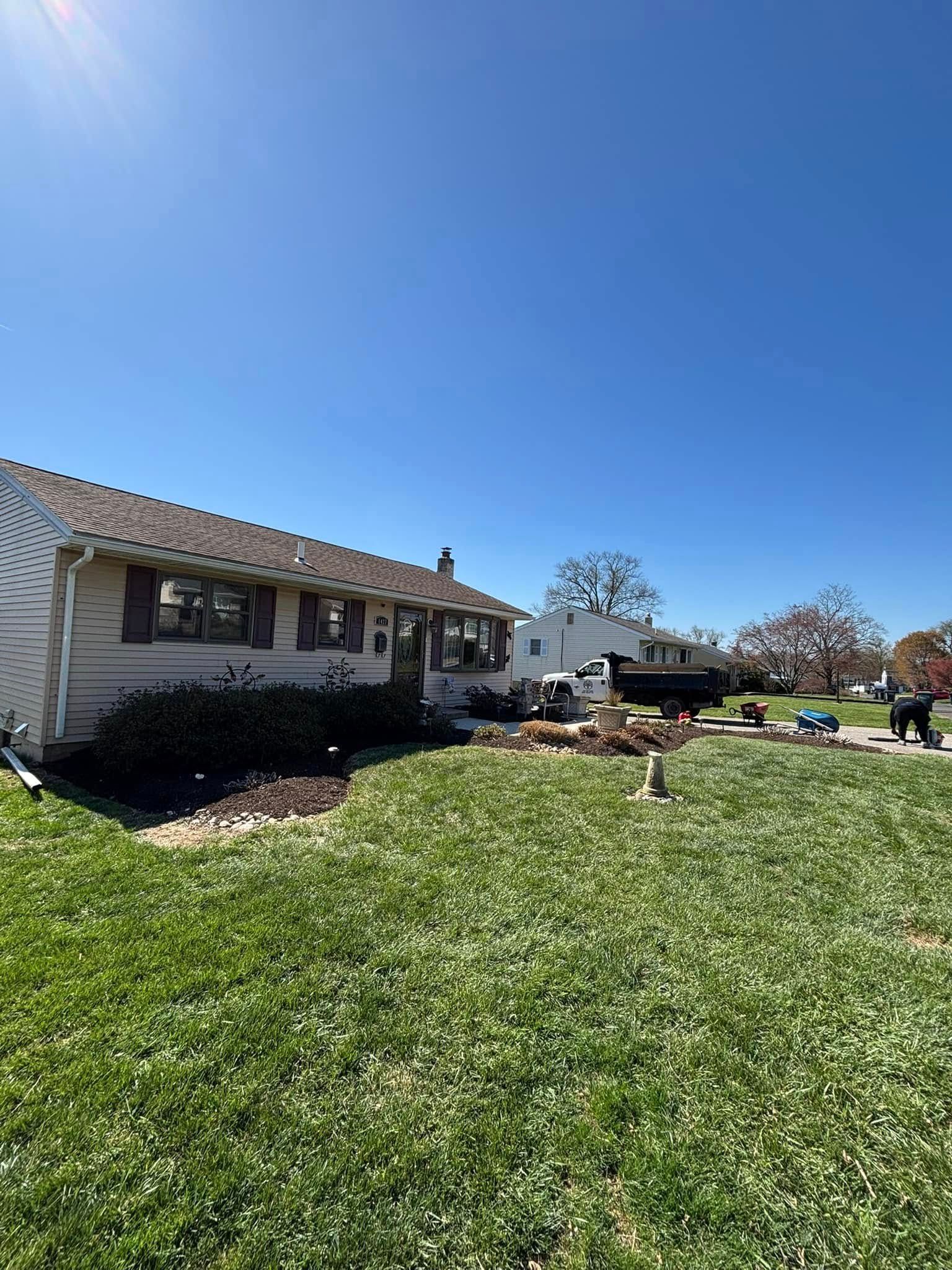 A beige house with a brown roof and shutters, a green lawn, and a clear blue sky.