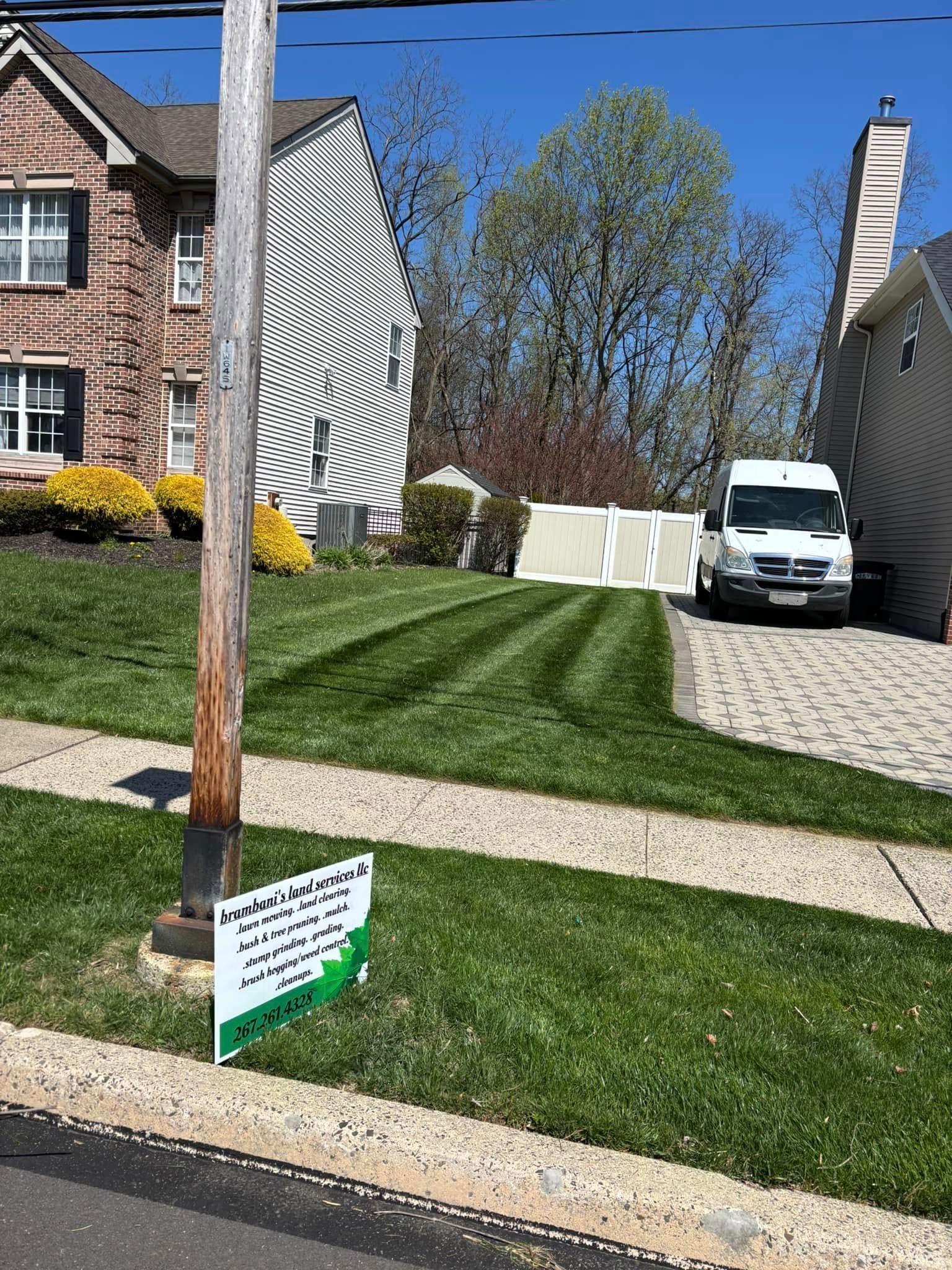 A well-mowed lawn in front of houses; a white van is parked. A sign sits in the yard.