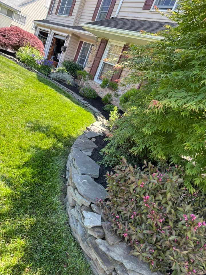Stone retaining wall with a landscaped garden next to a house with a green lawn.