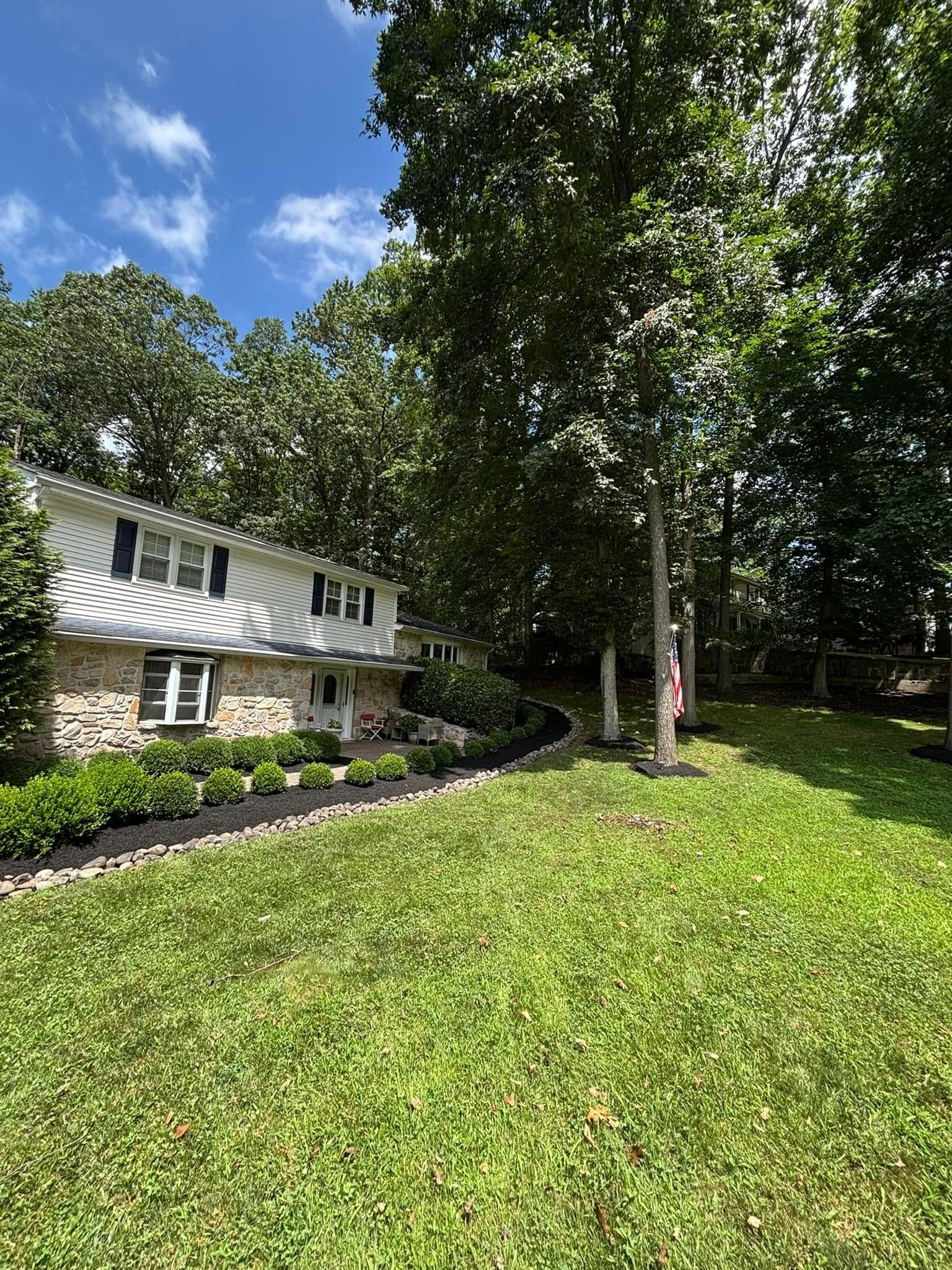 Two-story house with stone facade, surrounded by trees and green lawn under a partly cloudy sky.