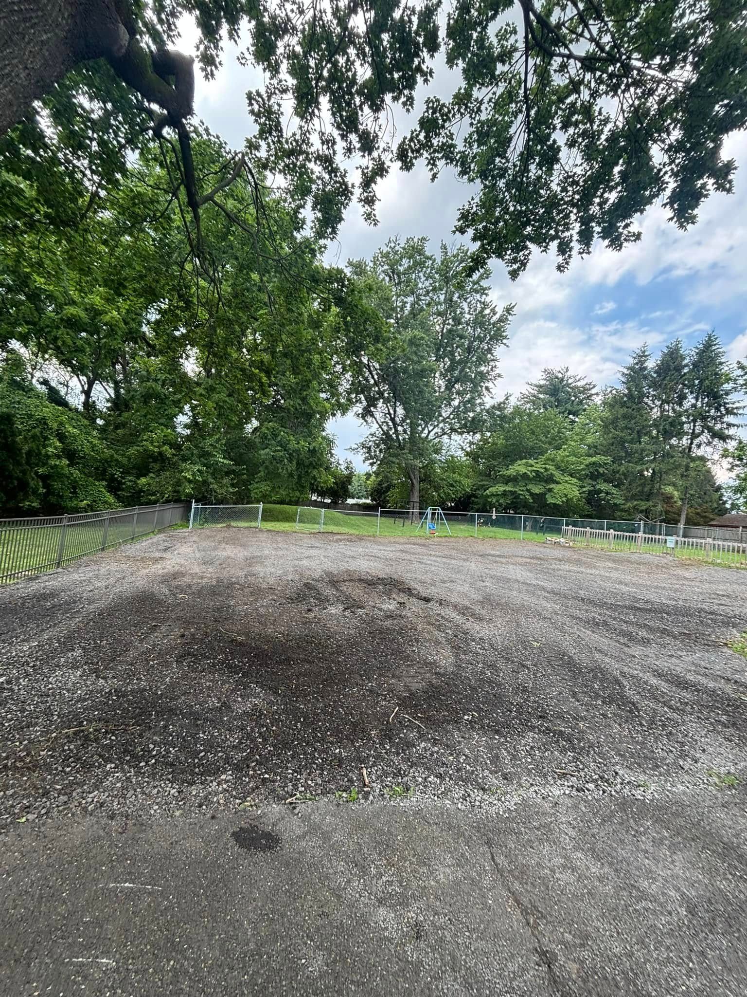 A pile of gray gravel in front of trees under a cloudy sky.