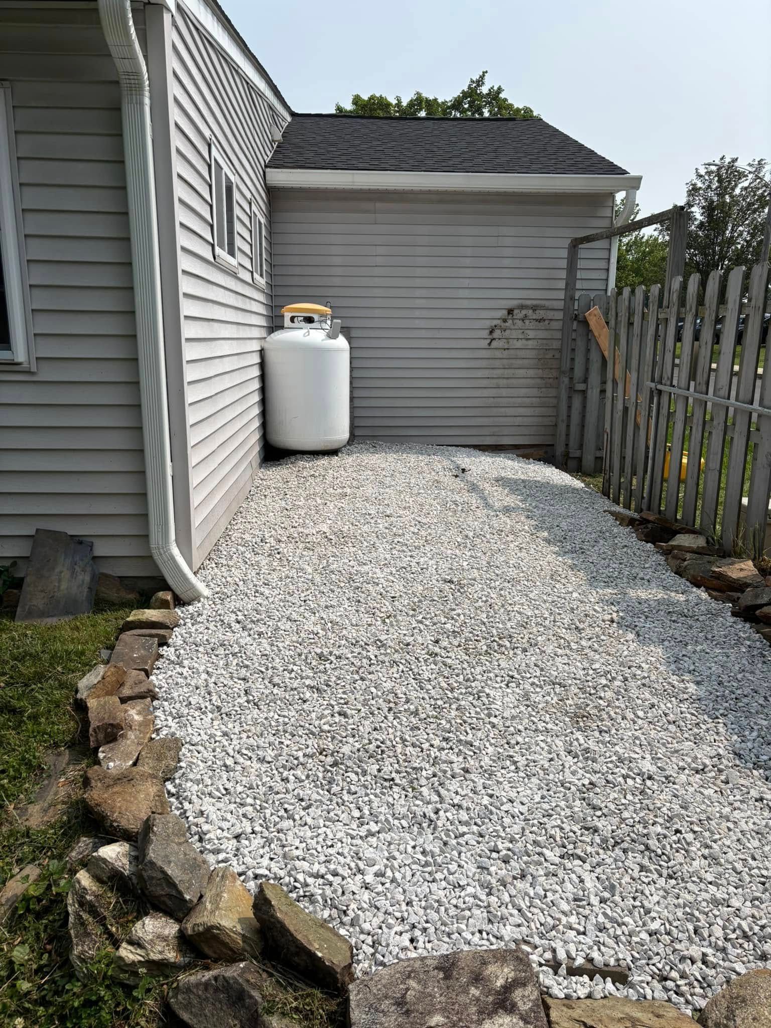 Backyard area with white gravel, propane tank, gray house, and fence.