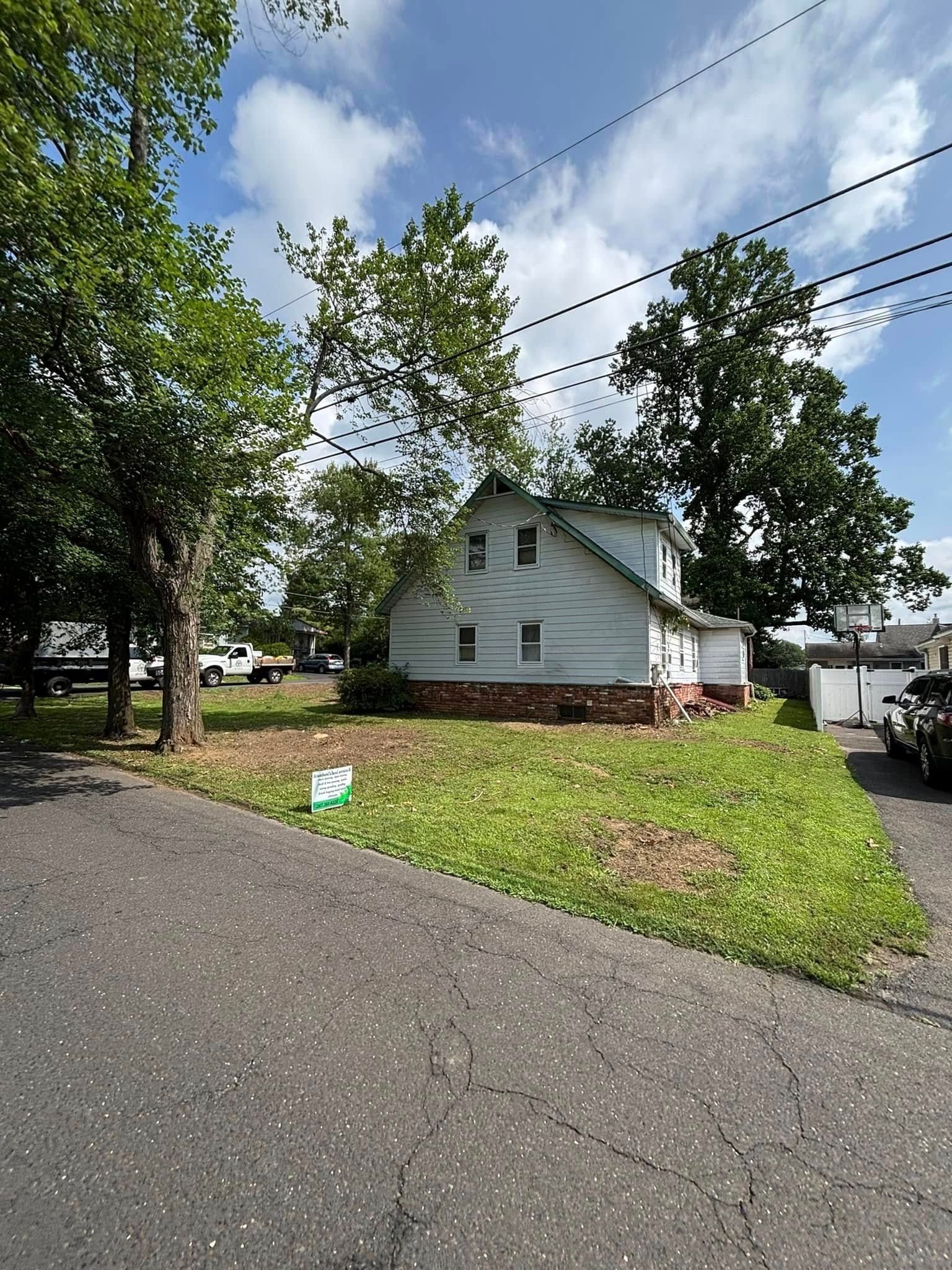 A small, light-blue house with brick base and trees on a grassy lot, viewed from a street.