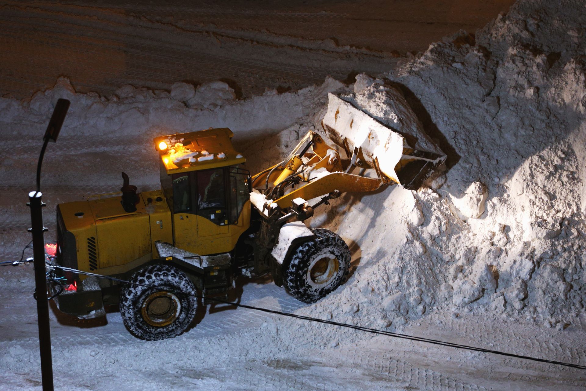 Yellow snowplow pushing a large snow pile at night.