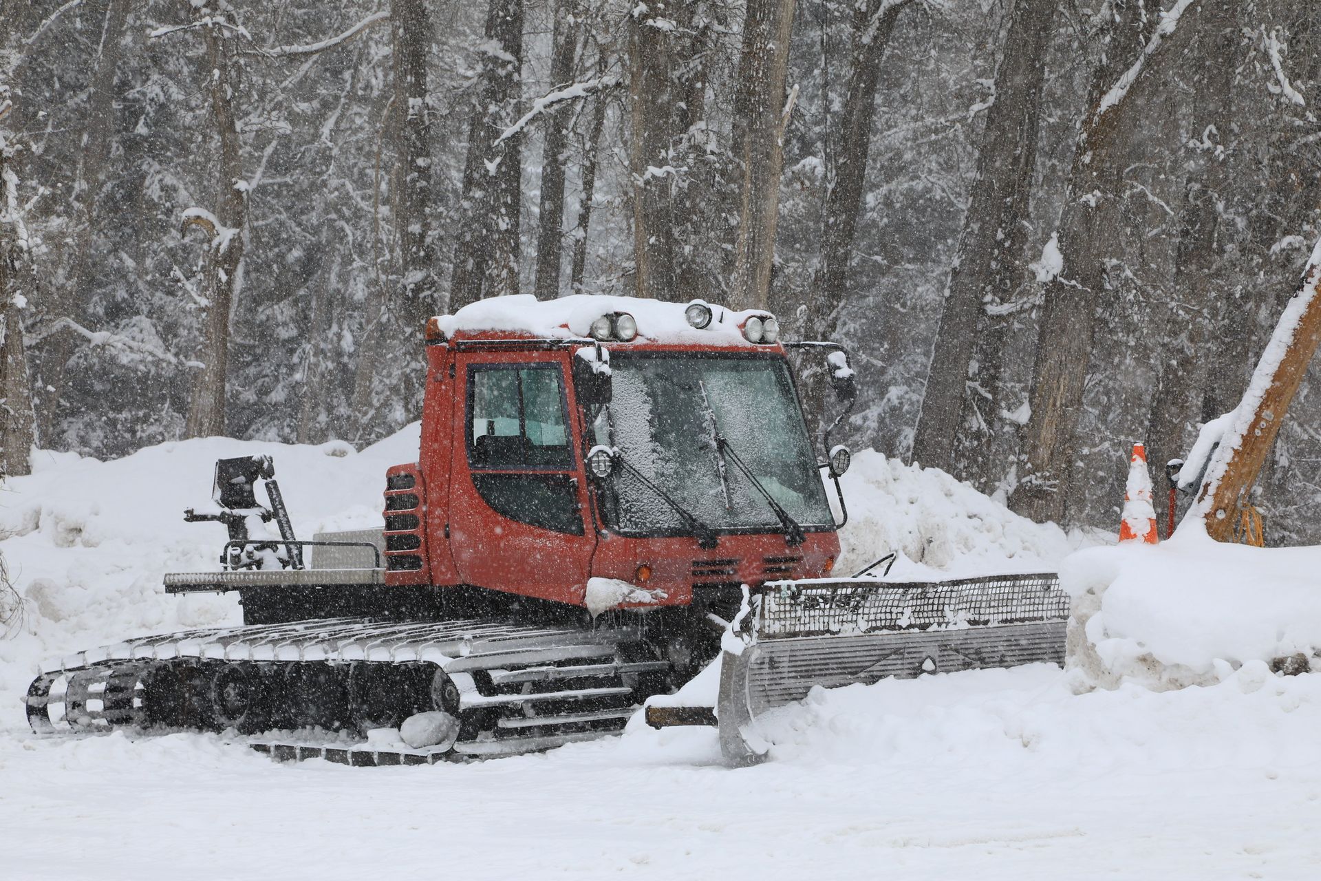 Red snowcat plowing snow on a snowy road near trees.