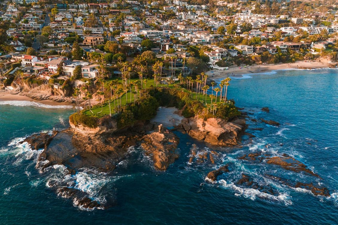 Classical Feng Shui. contact us An aerial view of a rocky cliff point with green trees jutting into a blue ocean, bordered by a coastal residential town.